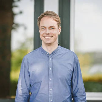 Junger Mann schut lächelnd in die Kamera.